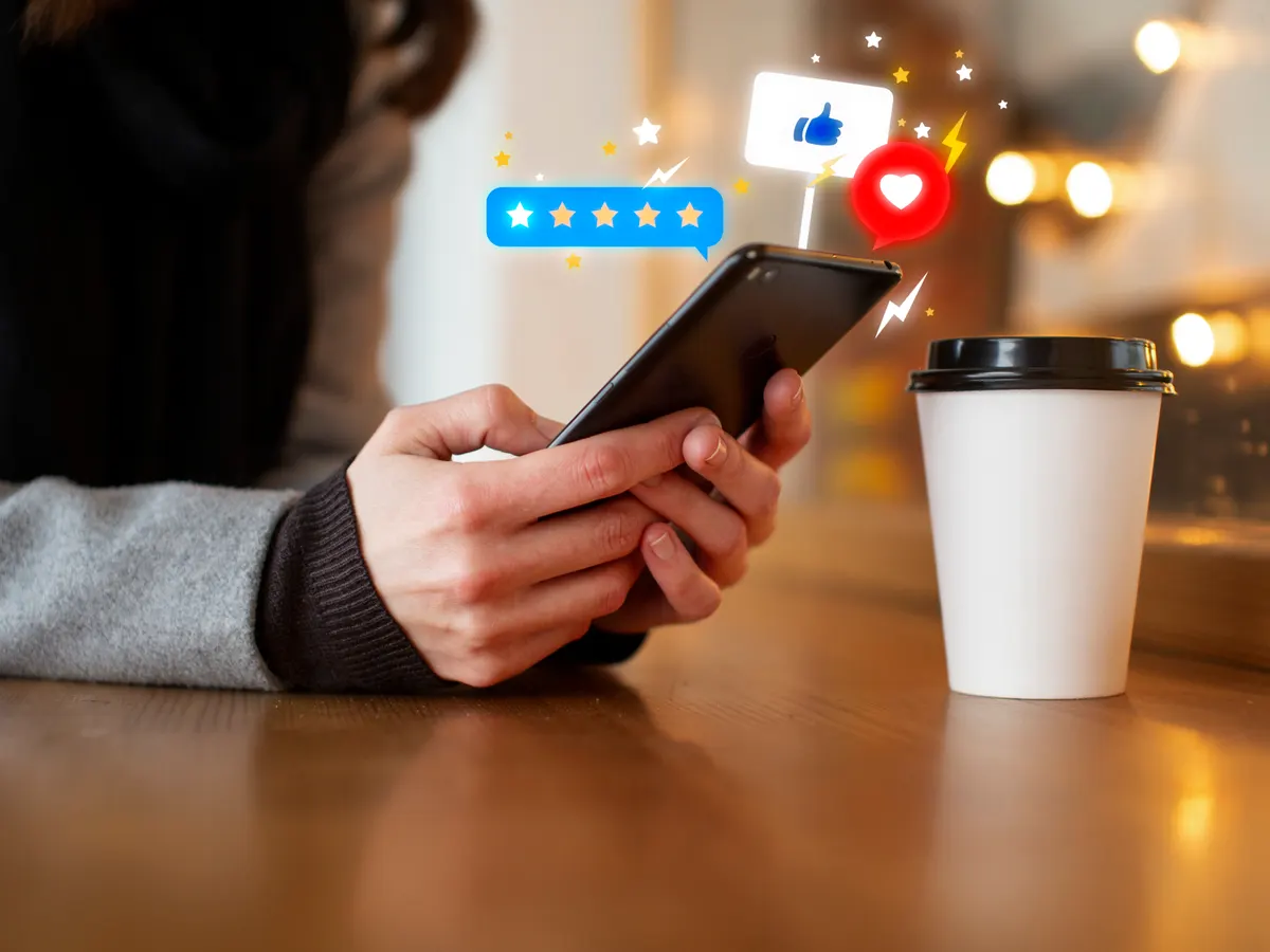 A customer leaving a five star review on a smartphone in a cafe
