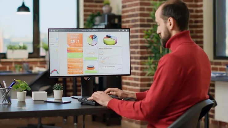 A man analyzing charts and reports on a desktop monitor in an office
