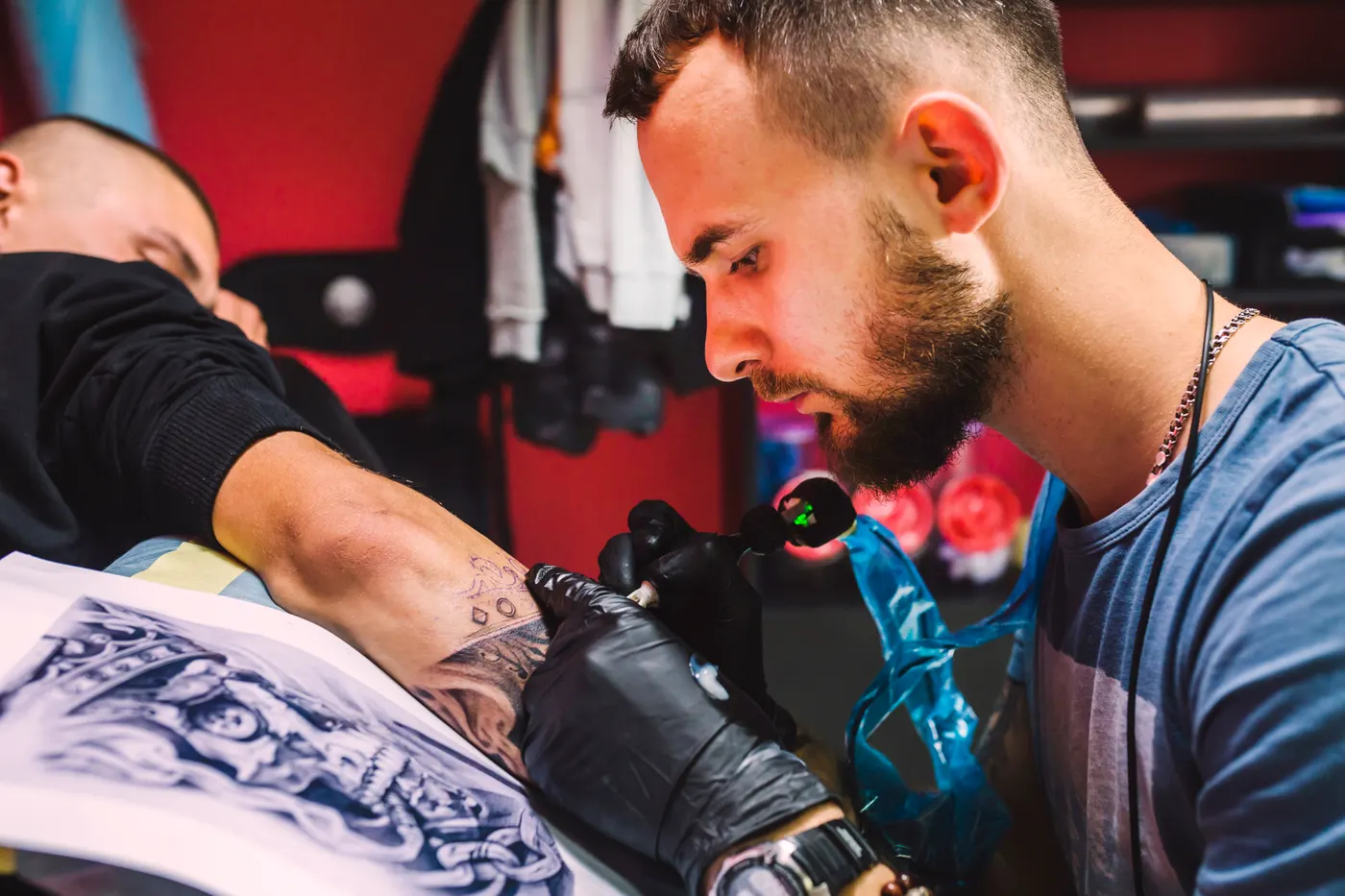 A tattoo artist working on a client's arm in a studio